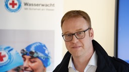 Peter Alsbach vor einem weißen Aufsteller der DRK Wasserwacht