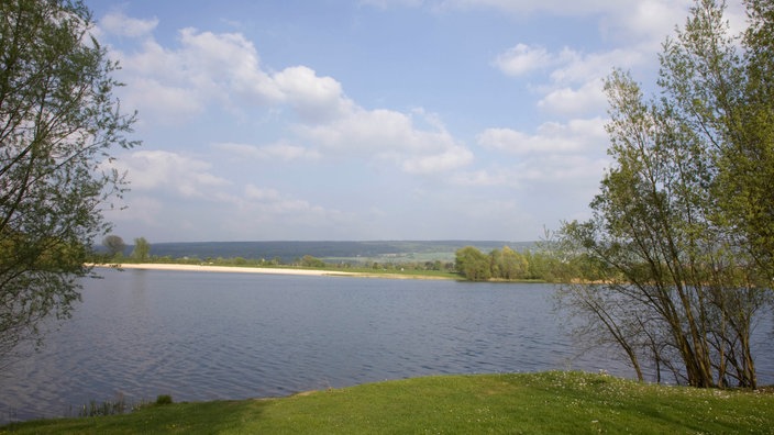Eine grüne Wiese, dahinter ein blauer See.