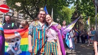 Julia und Rachel stehen vor einer Gruppe Menschen in bunter Kleidung.