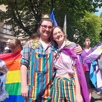 Julia und Rachel stehen vor einer Gruppe Menschen in bunter Kleidung.