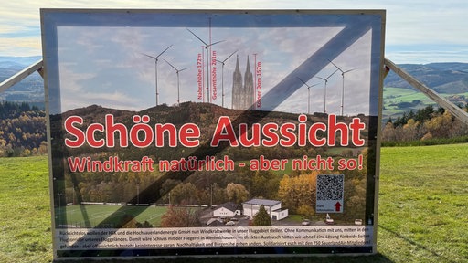 Ein Plakat gegen ein Windrad vor einer weiten Landschaft
