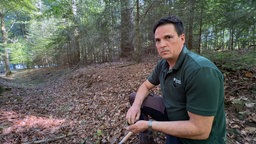 Ein Mann hockt mit einem Spaten im Wald 