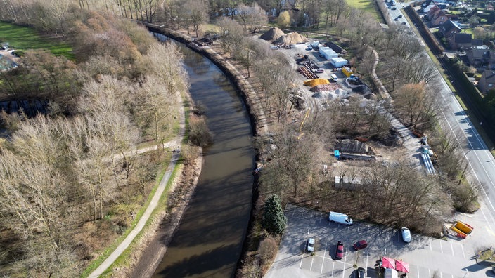 Aufnahme von der Ems von oben in Warendorf. Links von der Ems ist Grünfläche und rechts sind Parkplätze mit Bäumen drumherum.