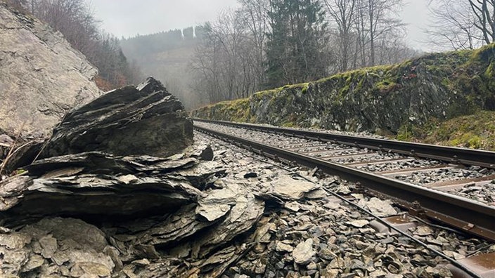 Ein großer Brocken Geröll liegt neben und zum Teil auf einer Bahnschiene