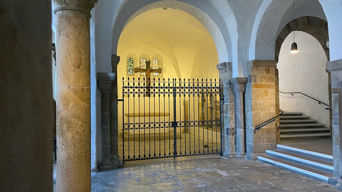Kellergewölbe mit einem abgesperrten raum, in dem ein großes Holzkreuz hängt 
