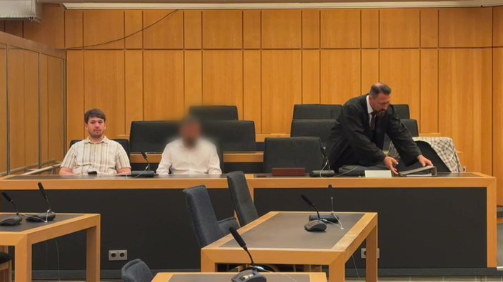 Das Bild zeigt die Anklagebank des Gerichtssaales mit dem Angeklagten und Verteidiger 