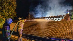 Zwei Feuerwehrleute löschen einen qualmenden  Dachstuhl