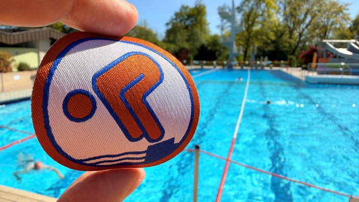 Ein Bronze-Schwimmabzeichen mit dem Freibad Verl im Hintergrund