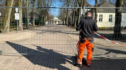 Ein Mann steht vor einem Bauzaun, der einen Bereich absperrt 