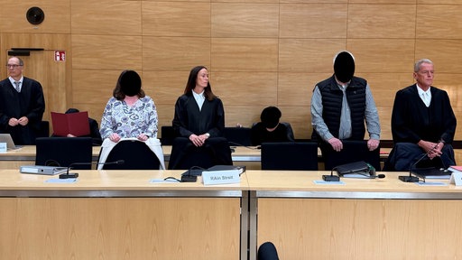Gerichtssaal in dem Anwälte und die Angeklagten stehen beziehungsweise sitzen