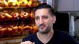 Ein Mann in Nahaufnahme, im Hintergund werden Hähnchen gegrillt.