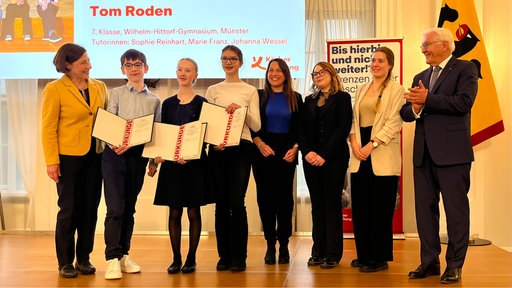 eine Gruppe von Schülerinnen und Schülern steht neben einer Lehrerin und dem Bundespräsidenten