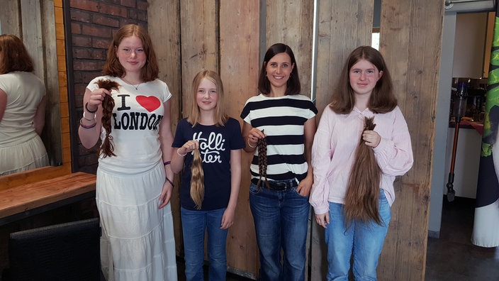 Von links aufgereiht stehen: Schülerin Cecilia (18), Schülerin Anna (11), Lehrerin Julia Schüßler, Schülerin Sophie (13). Alle halten ihre abgeschnittenen Haare in der Hand.
