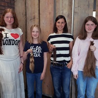 Von links aufgereiht stehen: Schülerin Cecilia (18), Schülerin Anna (11), Lehrerin Julia Schüßler, Schülerin Sophie (13). Alle halten ihre abgeschnittenen Haare in der Hand.
