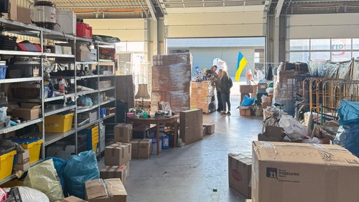 Drei Menschen stehen in einem Lager mit Spenden für die Ukraine