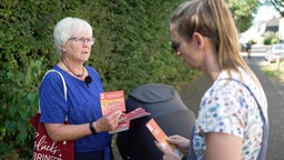 Eine Frau überreicht einer anderen Frau einen Flyer