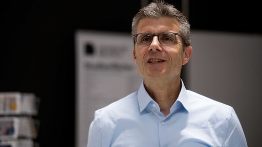 Dario Anselmetti lächelt in die Kamera. Er trägt ein hellblaues Hemd, eine Brille und hat graue Haare.