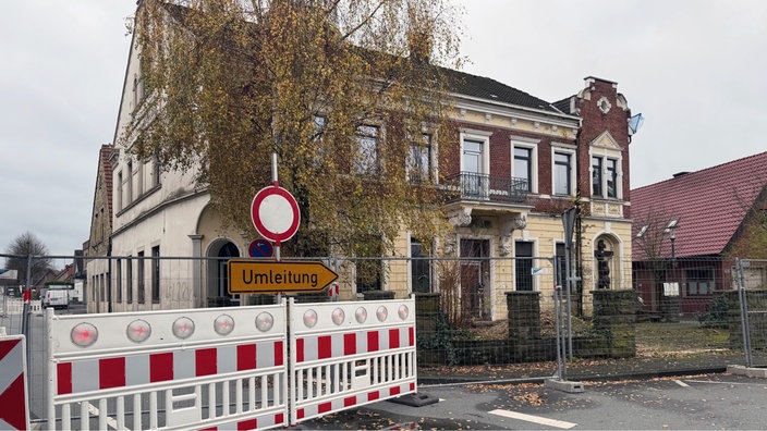 Vor einem alten Gebäude stehen ein Bauzaun und ein Umleitungsschild