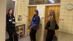 Mitarbeiterin des INDRO e.V. erklärt zwei Frauen etwas zum Konsumraum, in dem sie sich befinden.
