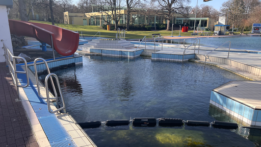 Ein Außenschwimmbecken mit Rutsche. Das Wasser ist sehr grünlich und dunkel.