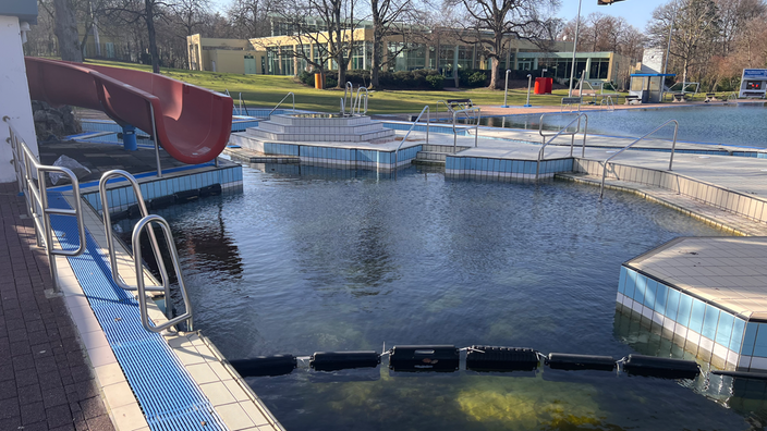 Ein Außenschwimmbecken mit Rutsche. Das Wasser ist sehr grünlich und dunkel.