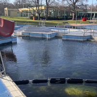 Ein Außenschwimmbecken mit Rutsche. Das Wasser ist sehr grünlich und dunkel.