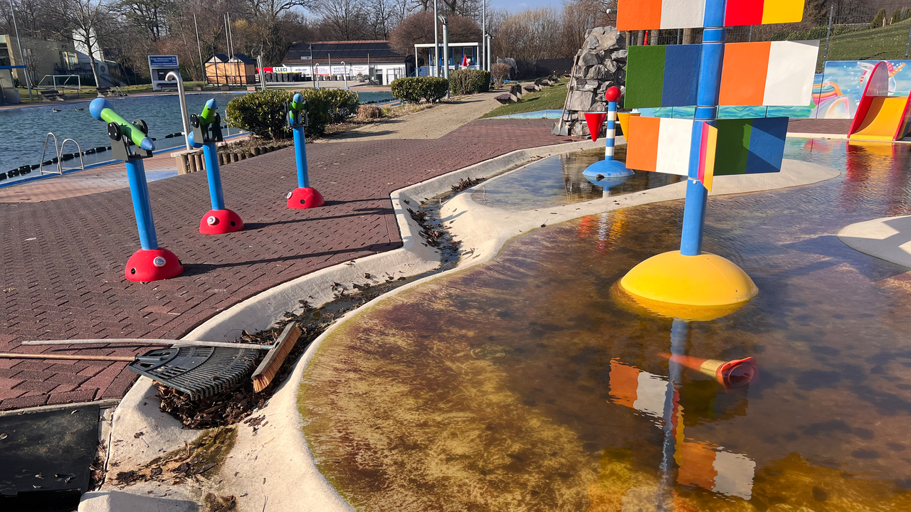 Ein Freibad mit mehrere Schwimmbecken. Das vordere Kinderbecken ist sehr verschmutzt und enthält bräunliches Wasser.