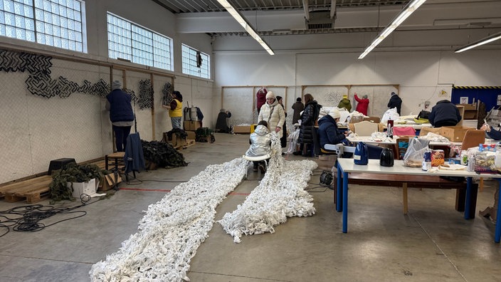 In einer Lagerhalle produzieren Ukrainerinnen und Ukrainer gemeinsam Tarnnetze in Bielefeld.