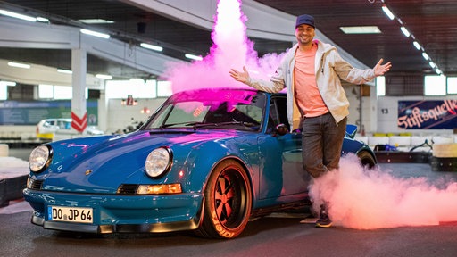 JP Kraemer vor einem blauen Sportwagen auf einer Bühne