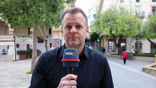 Ein Reporter mit WDR_Mikrofon schaut in die Kamera 