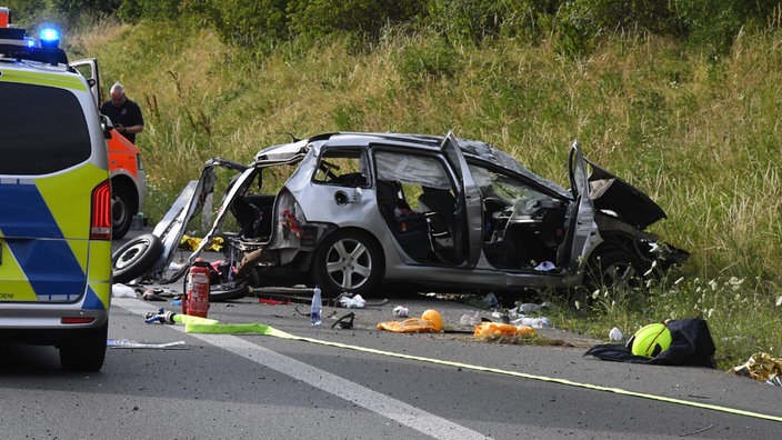Die Ruine eines sehr zerstörten Autos am Wegesrand, drumherum ein Feuerlöscher, Wasserflaschen, Plastik und andere Unfall-Reste