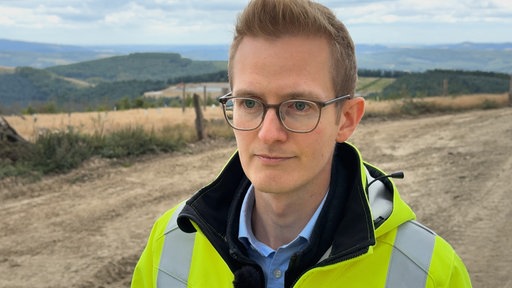 Ein Mann mit gelber Warnjacke steht auf einem Feld 