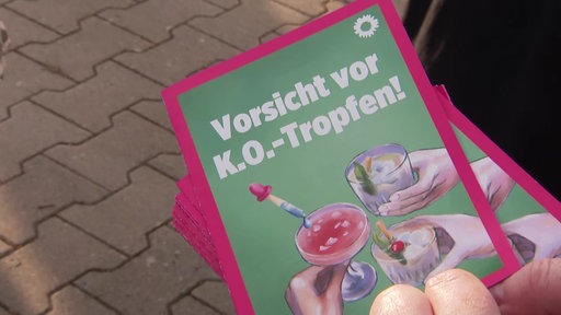Ein grüner Flyer, pink umrandet, mit der Aufschrift "Vorsicht vor K.O.-Tropfen!" 