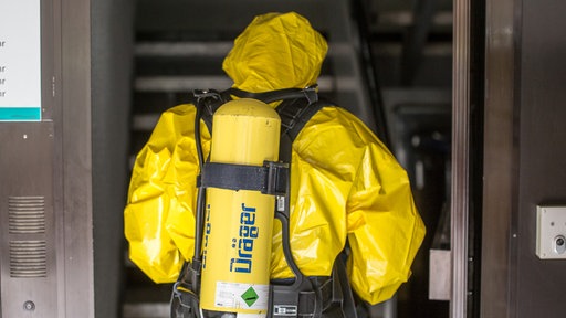 Ein Mann der Feuerwehr steht im Eingang eines Mehrfamilienhauses, gekleidet in einen Schutzanzug für Gefahrengüter