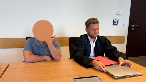 Zwei Männer sitzen an einem Tisch und blicken nach unten.
