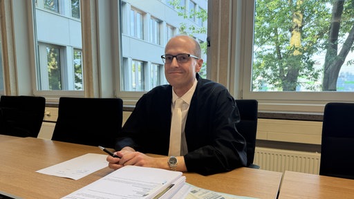 Ein Mann mit Robe sitzt lächelnd an einem Tisch