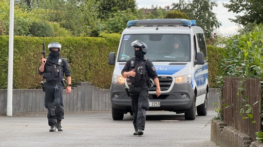 Einsatzkräfte des SEK gehen vor einem Polizeiwagen entlang