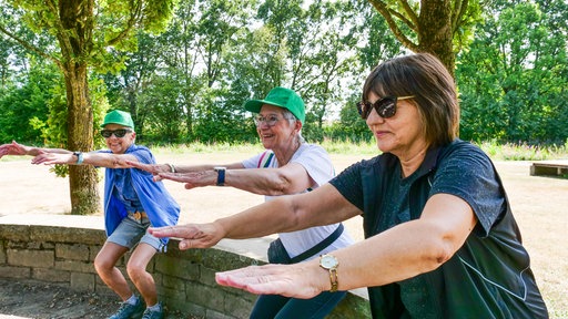 Drei Frauen machen Kniebeugen in einem Park.