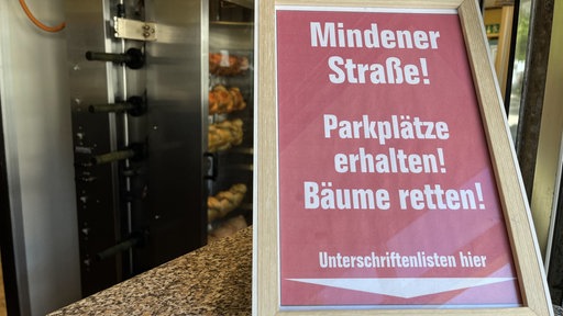 Ein Schild auf den Tresen vom Impiss mit dem Aufruf die parkplätze und Bäume zu erhalten
