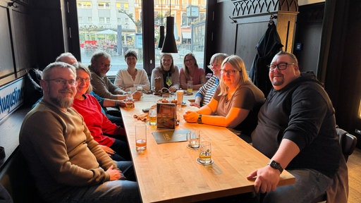 Eine Gruppe an Menschen sitzt an einem Tisch und trinkt Bier.