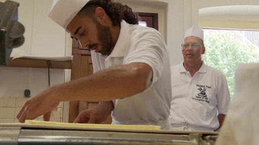 Ahmads Chef schaut ihm über die Schulter während er gerade Blätterteig faltet.