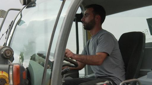 Hogir sitzt in einem Bagger und läd Mulch auf einen Transporter auf.