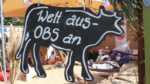 Auf einem Schild in Form einer Kuh steht: "Welt aus - OBS an".
