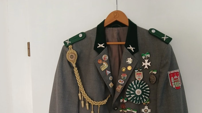 Eine Schützenjacke mit vielen Abzeichen hängt an einem Kleiderhaken