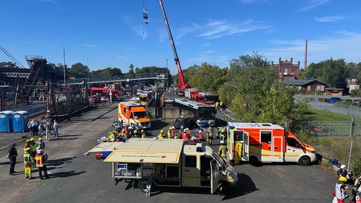 Auf einem größeren Platz sind Rettungswagen und ein Wagen vom Roten Kreuz aufgebaut mit vielen Rettungskräften auf diesem Platz.