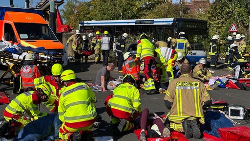 Während im Hintergrund ein Bus steht, stehen viele Einsatzkräfte auf dem Platz.