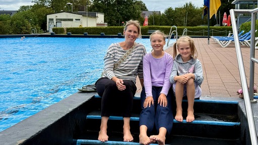 Eine Mutter mit zwei kleinen Kindern vor einem Schwimmbecken