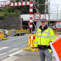 Egon Hasse steht mit einer Flagge vor der höhenbegrenzten Baustelle der Eisenbahnbrücke in Lügde