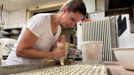 Bäckerlehrling Ann-Kathrin Lüttmann spritzt die Butter mit einem Spritzbeutel auf den Teig, daraus wird Butterkuchen.