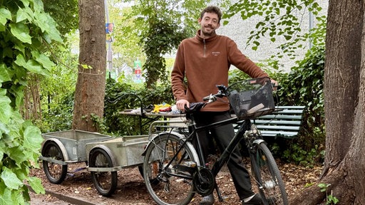 Konstantin Wodowos steht hinter seinem Fahrrad an dem zwei Anhänger befestigt sind.